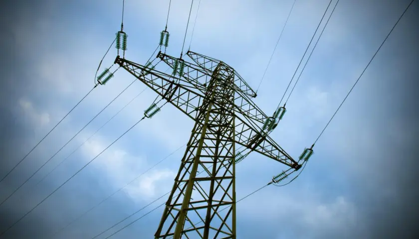 Wysoki słup energetyczny z przewodami, pod niebem pełnym chmur. Mam nadzieję, że nie będzie awarii, bo wtedy czeka nas bonifikata za brak prądu.