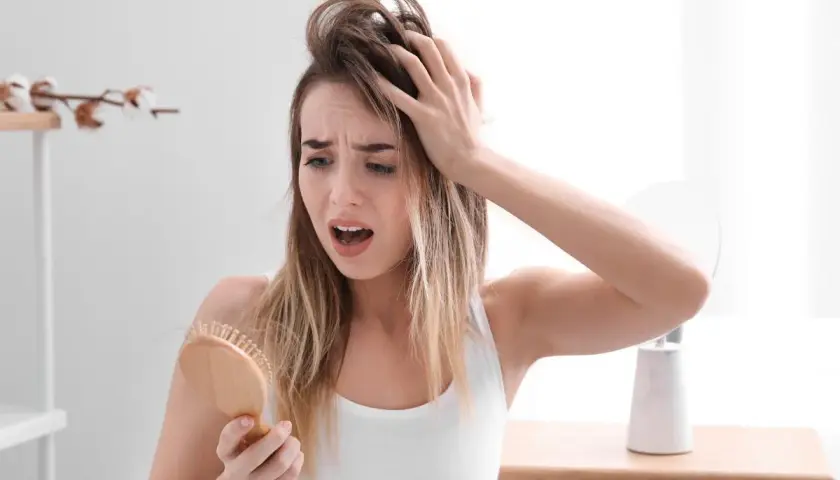 Mujer preocupada por la caida de pelo en verano, con mechones en el cepillo.