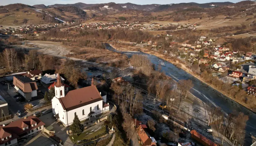 Widok z lotu ptaka na malowniczą dolinę Popradu zimową porą. Biały kościół z czerwoną wieżą góruje nad zabudowaniami.