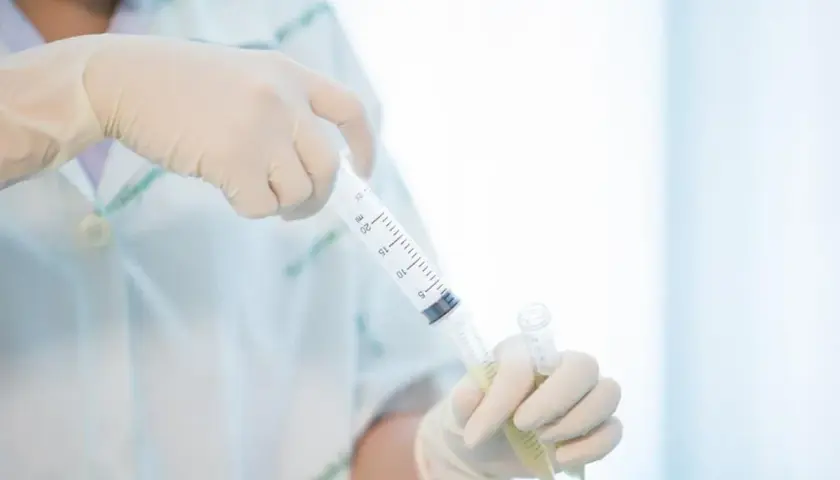 Ręce w rękawiczkach trzymają strzykawkę z płynem i probówkę.