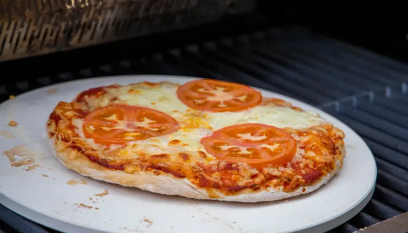 Eine Margherita-Pizza mit Tomatenscheiben und geschmolzenem Käse wird auf einem Pizzastein im Backofen gebacken.