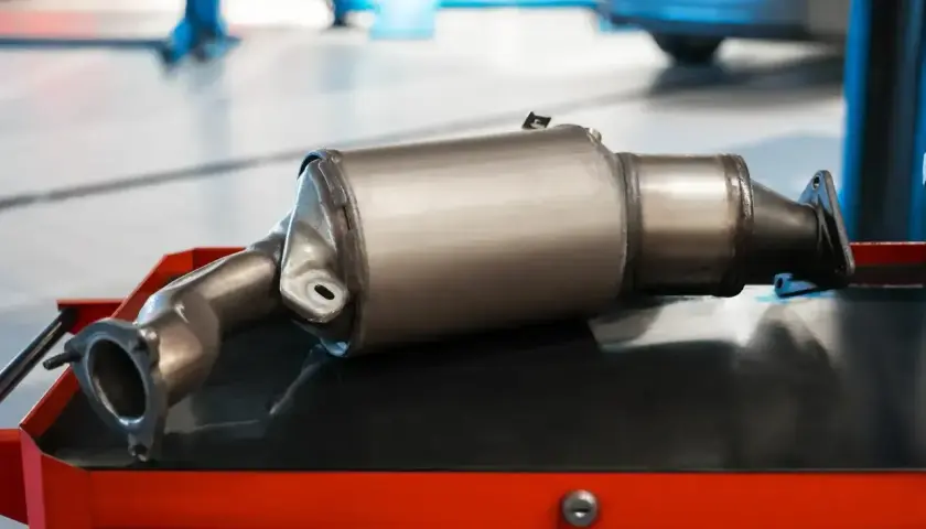 Nowy katalizator samochodowy, czyli GPF (Gasoline Particulate Filter), leży na wózku warsztatowym.
