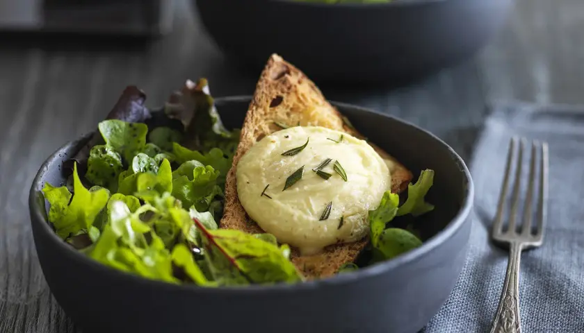 Salade fraîche avec une tranche de pain grillé et une quenelle de **chèvre chaud** garnie d'herbes.