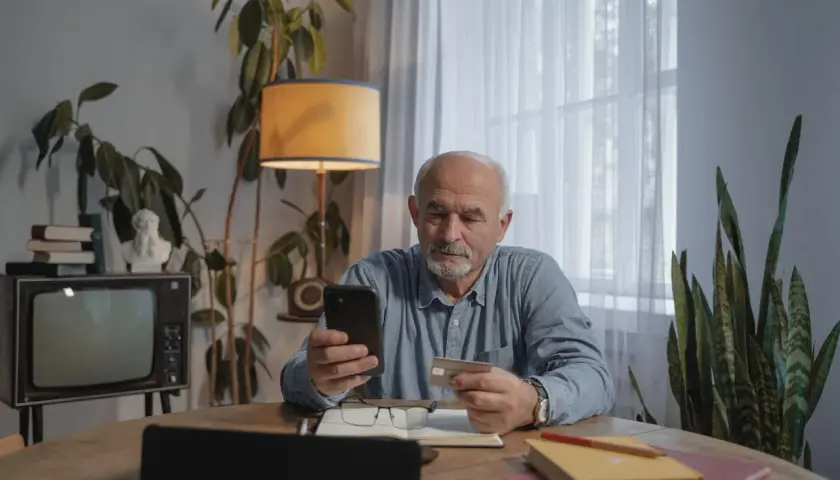 Starszy pan sprawdza w telefonie, ile kosztuje przedłużenie w lombardzie.