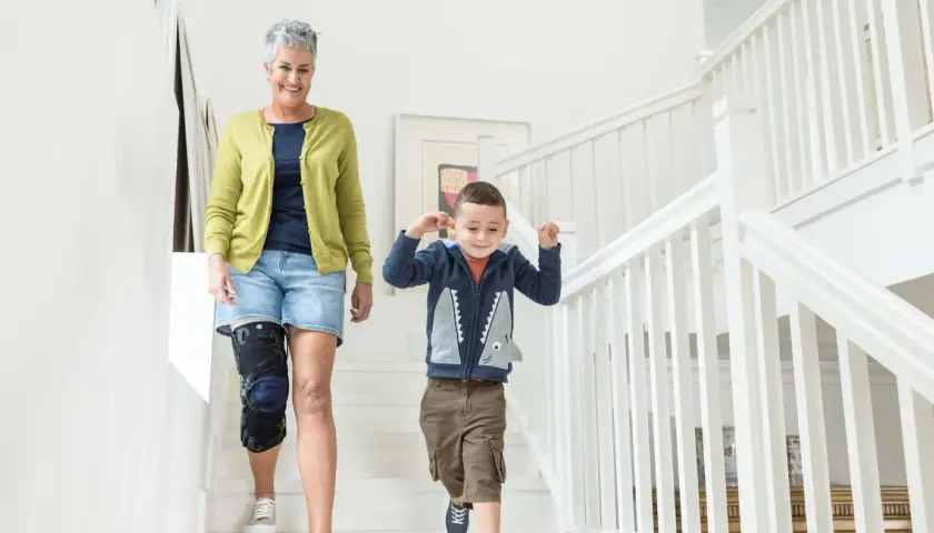Frau mit Kniebandage, die mit ihrem Enkel die Treppe hinuntergeht. Einlagen bei Kniearthrose können helfen, die Mobilität zu verbessern.