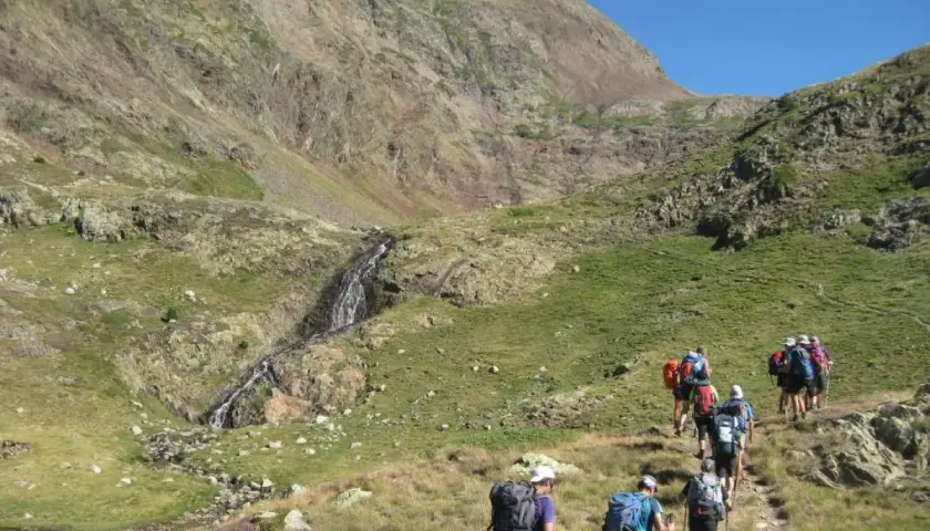 Senderistas caminan por un sendero de montaña hacia una cascada, como si fuera la porta del cel.