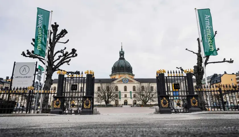 Grön flagga med texten "Armémuseum" vid krigsmuseum Stockholm. Imponerande byggnad med kupol och staket.