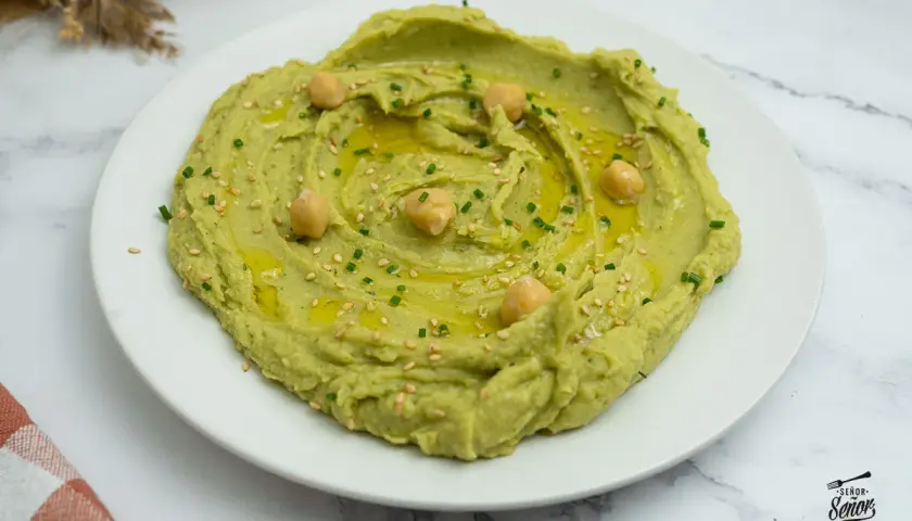 Hummus de aguacate cremoso, decorado con garbanzos, aceite de oliva, semillas de sésamo y cebollino. ¡Un entrante delicioso!