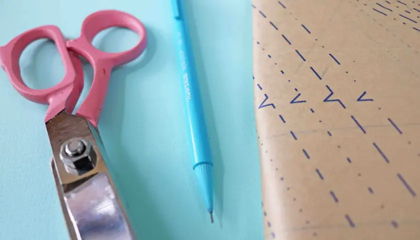 Pink scissors and a blue pen lie next to a piece of pattern paper, ready for a project to place on fold.