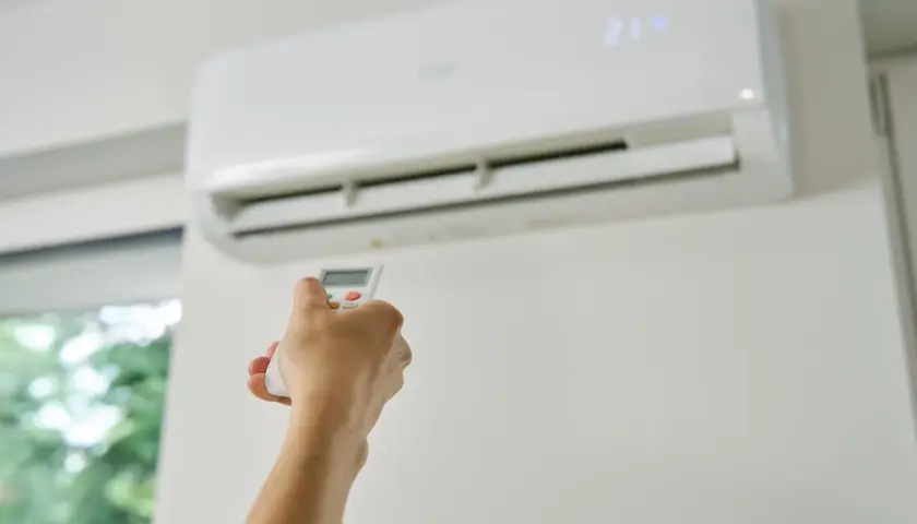 Dłoń trzymająca pilot do klimatyzacji, która chłodzi pomieszczenie. Zastanawiasz się, czy klimatyzacja pobiera dużo prądu?