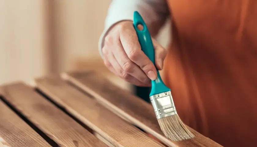 Mano con brocha lijando listones de madera barnizada para restaurar un mueble.