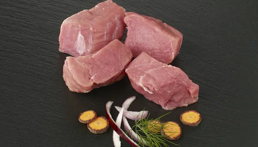 Quatre morceaux d'épaule de veau crus, accompagnés de rondelles de carottes, d'oignon rouge et d'aneth sur fond noir.