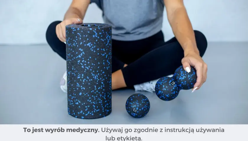 Kobieta siedzi obok wałka i piłek do rolowania mięśni.