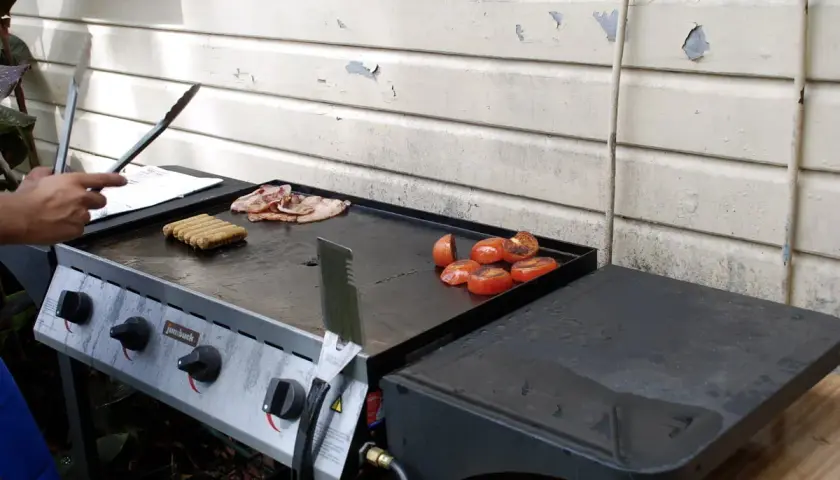 Comment allumer plancha gaz : des saucisses, du bacon et des tomates grillent sur la plaque.