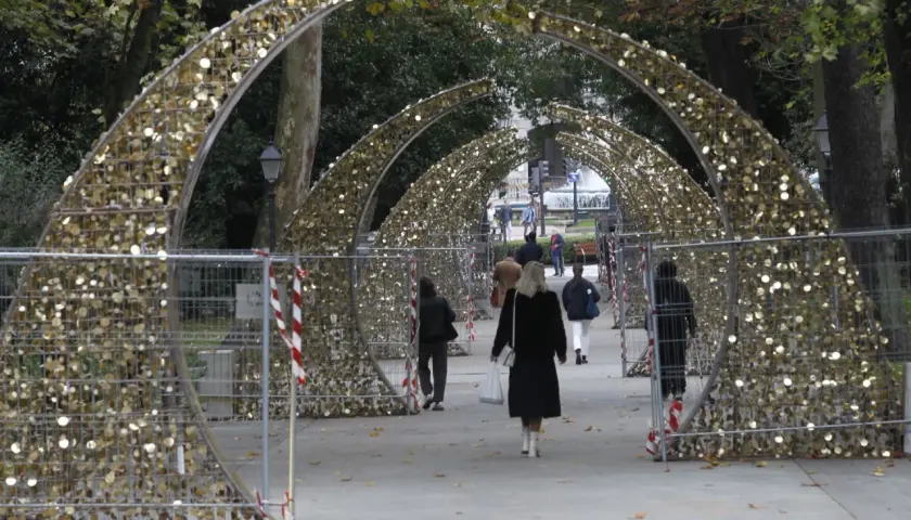 Personas pasean bajo arcos dorados decorados con luces, preparándose para el encendido de luces en Oviedo.