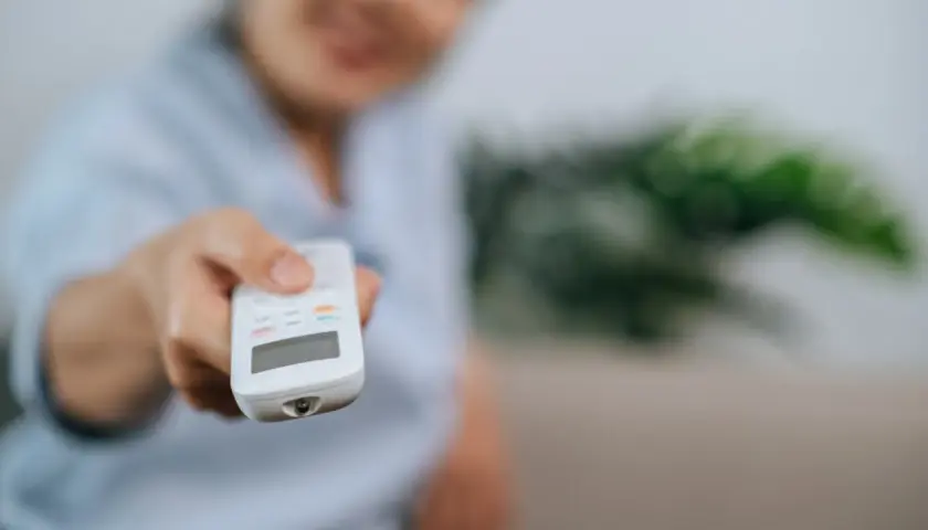 Persona sonriente ajusta el aire acondicionado con el mando. Controla la potencia aire acondicionado kw para un confort ideal.