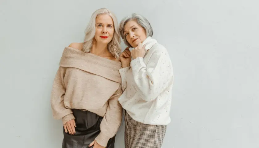 Deux femmes élégantes, l'une en pull beige dénudant ses épaules et jupe en cuir, l'autre en pull blanc et jupe à carreaux, prouvent qu'il n'y a pas d'erreurs de style qui vieillissent.