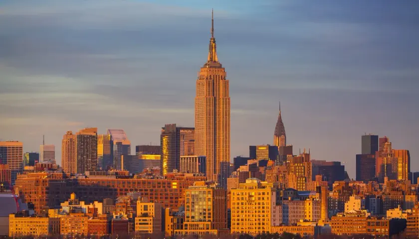 Zachód słońca nad Manhattanem. Widać Empire State Building i Chrysler Building. Zastanawiasz się, ile się leci do Nowego Jorku?