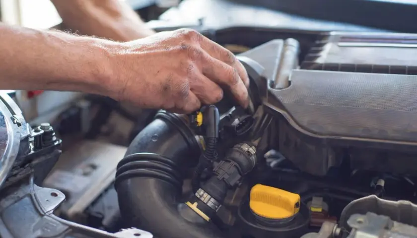 Ręce mechanika pracujące przy silniku samochodu, widoczne przewody i żółta zakrętka.