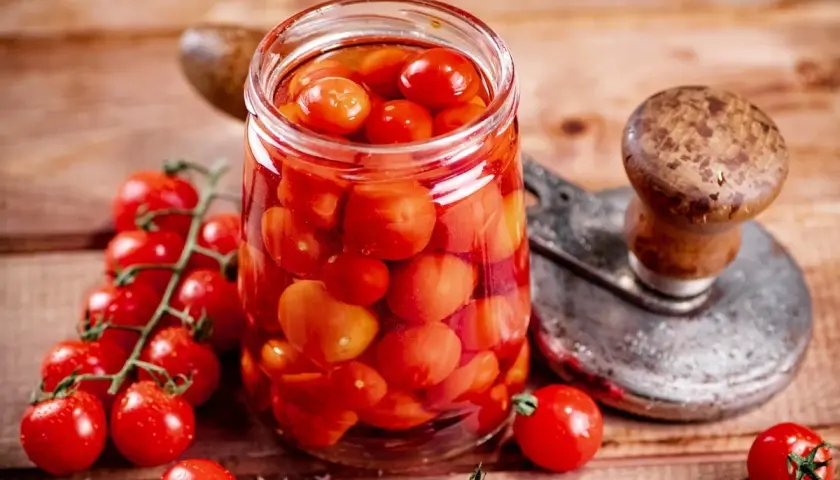 Glas voller Tomaten, bereit zum Einkochen wie Oma. Frische Kirschtomaten und ein Einkochgerät auf Holzuntergrund.