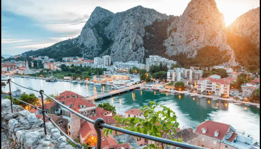 Widok na miasteczko Omiš w Chorwacji, z rzeką Cetiną i górami w tle. Słońce zachodzi nad malowniczą **Dalmacją**.