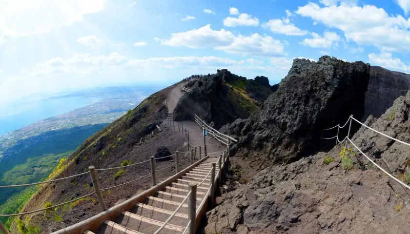 Sentiero sul cratere del Vesuvio, un vulcano attivo. Scale di legno e corde guidano i visitatori verso la cima, con vista sul golfo.