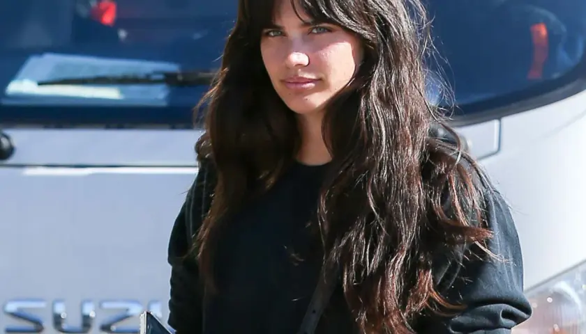 Mujer con cabello largo y oscuro, luciendo un moderno flequillo cortina, mira a la cámara mientras sostiene un teléfono.