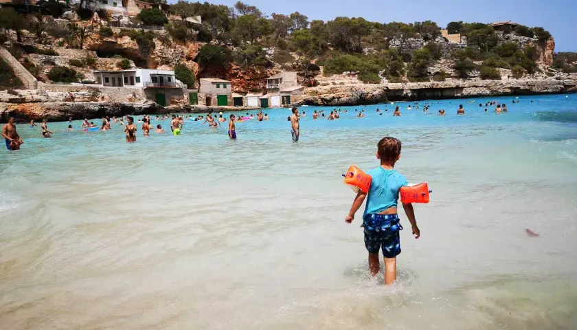 Sonnige Bucht mit vielen Menschen, ein kleiner Junge mit Schwimmflügeln geht ins Meer. Perfekte urlaubsziele mit kindern.