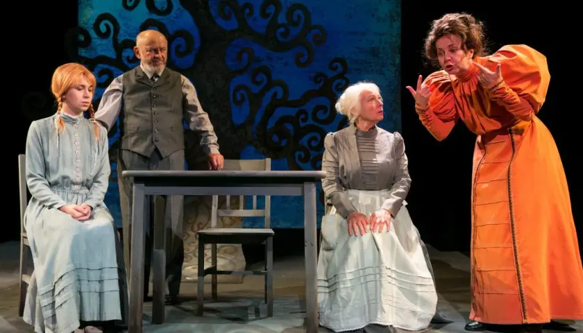 Scena z Teatru Groteska. Cztery postacie w strojach z epoki, w tym młoda dziewczyna, starszy mężczyzna i dwie kobiety, rozmawiają przy stole.
