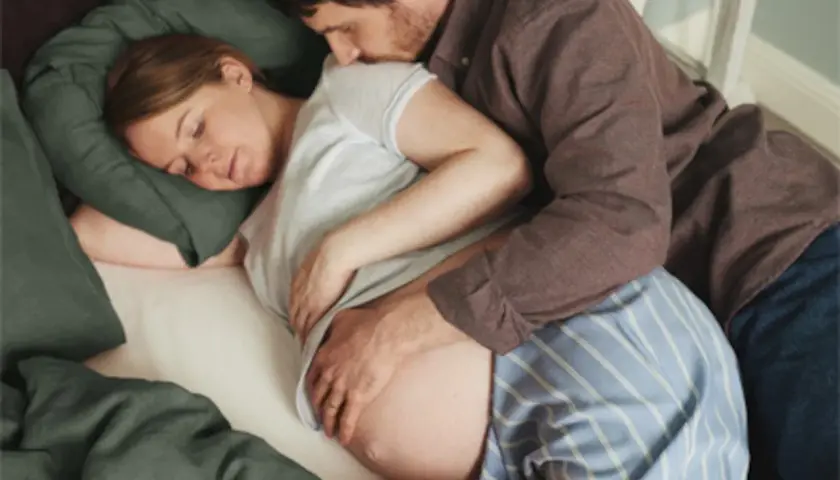 En man kramar en gravid kvinna som sover. Hans hand vilar på hennes mage, ett tecken på lyckad hinnsvepning och förväntan inför barnets ankomst.