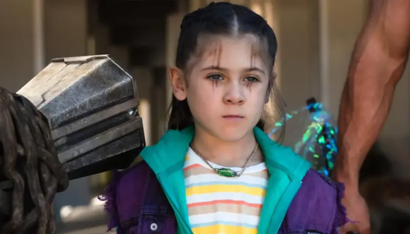 La fille de Thor, avec des marques sur le visage, porte une veste violette et un collier vert. À côté d'elle, le marteau Mjolnir.