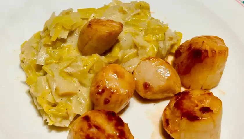 Saint-Jacques poêlées sur un lit de fondue de poireaux crémeuse, un plat savoureux et réconfortant.