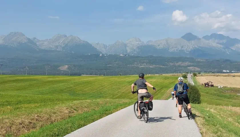 Rowerzyści przemierzają malowniczą trasę. W tle rozciągają się majestatyczne Tatry, tworząc piękny historyczno kulturowo przyrodniczy szlak wokół gór.