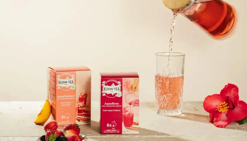 Kusmi Tea AquaRosa i AquaSummer w pudełkach, nalewanie różowej herbaty do szklanki. Obok owoce i hibiskus.