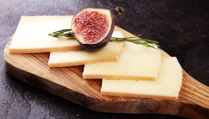 Tranches de fromage à raclette sur planche en bois, garnies d'une figue coupée et de romarin. Parfait pour une recette raclette 6 personnes.