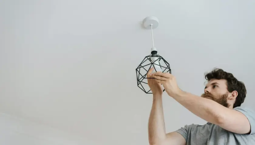 Mężczyzna dokonuje wymiany żarówki led w oprawie sufitowej. Nowe światło rozjaśni wnętrze.