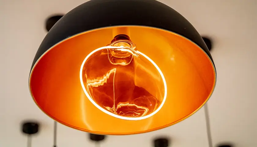 Lámpara colgante moderna con interior dorado y una bombilla decorativa Edison encendida, creando un ambiente cálido.