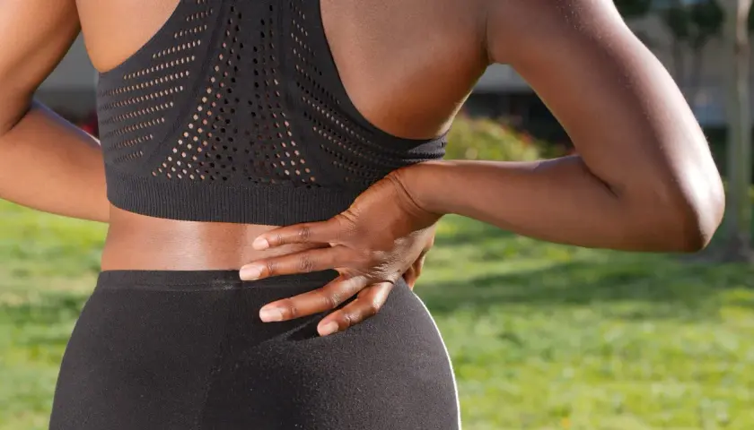Une femme en tenue de sport ressent une douleur barre dans le dos, sa main posée sur la zone sensible.