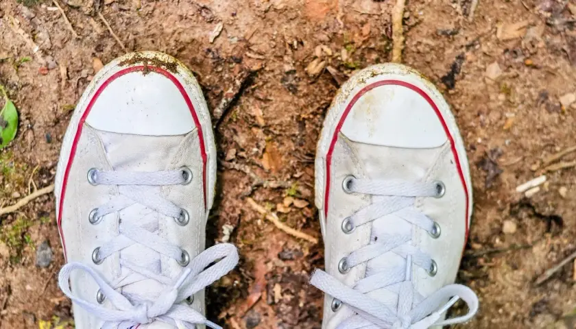 Białe trampki z czerwonymi akcentami, lekko zabrudzone ziemią, czekają na czyszczenie.