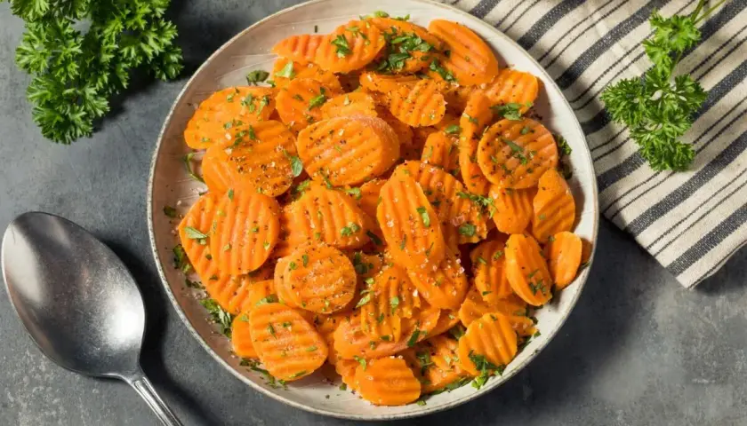 Carottes Vichy coupées en rondelles, saupoudrées d'herbes et de poivre, servies dans un plat avec une cuillère.