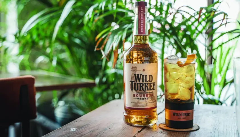 Un bicchiere di cocktail con bourbon Wild Turkey, ghiaccio e scorza d'arancia, accanto alla bottiglia.