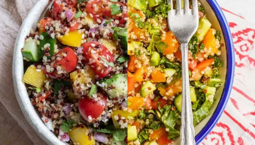 Ensalada de quinoa vibrante con tomates, pepino, pimientos y hierbas frescas. Un tenedor plateado descansa sobre la colorida mezcla.
