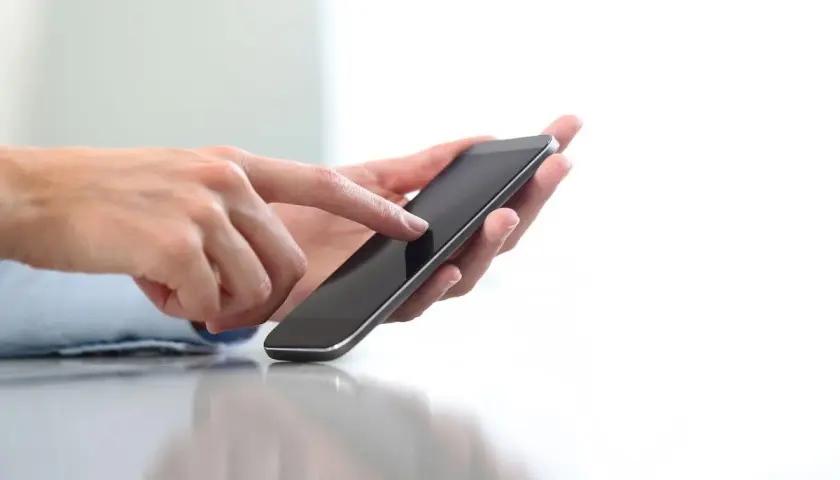 Dłonie trzymające smartfon, palec wskazujący dotyka ekranu. Szybko dowiesz się, jak doładować komuś konto ze swojego telefonu.