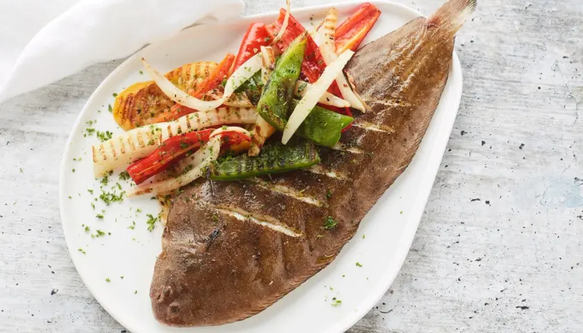 Sole grillé, garni de poivrons et d'oignons grillés, saupoudré de persil frais. Un plat savoureux et coloré.