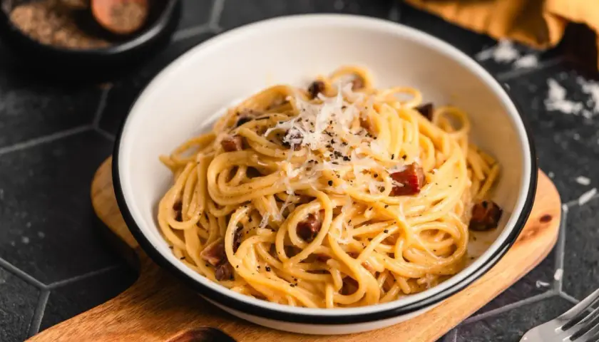 Ein Teller Spaghetti mit cremiger Sauce, garniert mit geriebenem Parmesan und schwarzen Pfefferkörnern. Darin versteckt sich leckerer Schinken für die perfekte Schinken Carbonara.