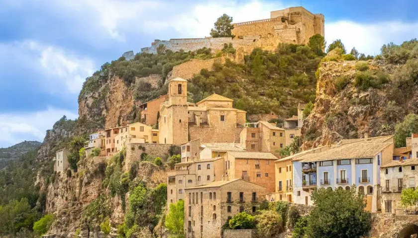 Pueblo de cambrils de muntanya aferrat a un penya-segat rocós, amb cases de colors i un castell imponent al cim.