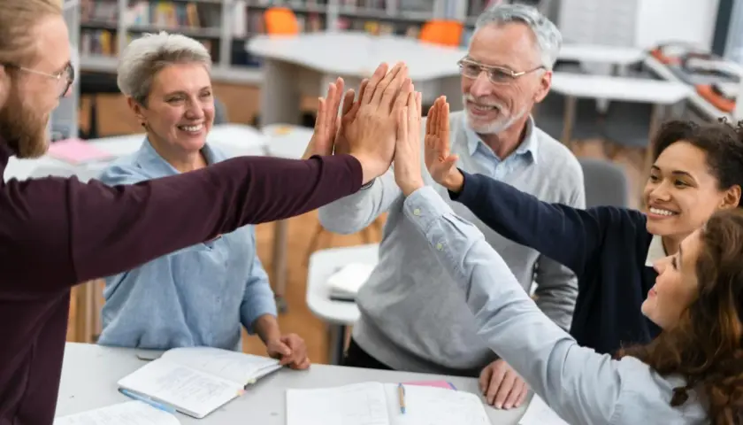 Lehrerteam gibt sich High-Five, um Burnout-Symptome zu bekämpfen. Freude und Zusammenhalt im Klassenzimmer.