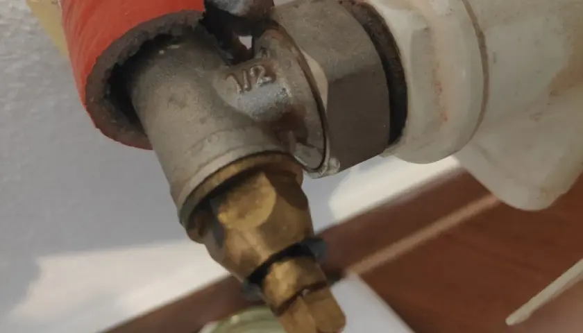 Zbliżenie na metalowy zawór grzejnikowy z oznaczeniem 1/2, częściowo osłonięty czerwonym materiałem.