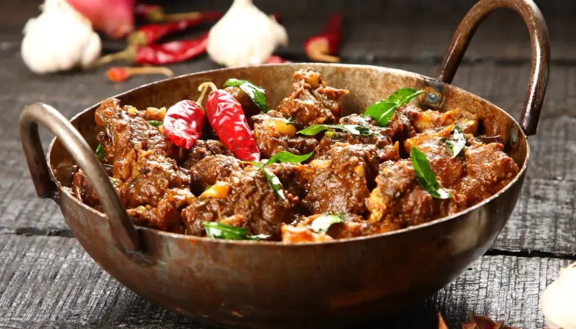 Aromatyczny gulasz z jagnięciny w miedzianym naczyniu, ozdobiony papryczkami chili i liśćmi curry.