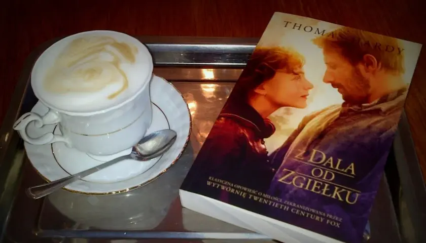 Kawa z pianką i książka Thomasa Hardy'ego "Z dala od zgiełku" na tacy. Idealny zestaw na spokojne popołudnie.